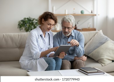 Female Professional Doctor Showing Medical Test Result Explaining Prescription Using Digital Tablet App Visiting Senior Man Patient At Home Sitting On Sofa. Elderly People Healthcare Tech Concept.