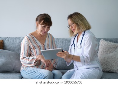 Female Professional Doctor Showing Medical Test Result Explaining Prescription Using Digital Tablet App Visiting Senior Woman Patient At Home Sitting On Sofa. Elderly People Healthcare Tech Concept.