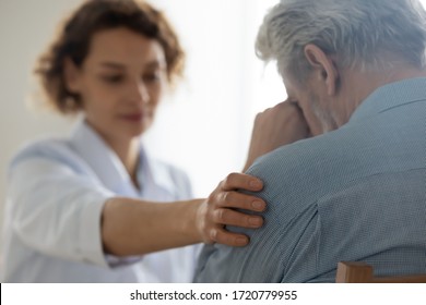 Female professional doctor touching shoulder comforting upset senior patient having geriatric disease expressing trust, support concept. Geriatrician helping lonely elderly crying man. Close up view