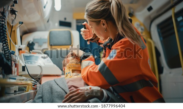 Female Professional EMS Paramedic Ride to\
Healthcare Hospital with Injured Patient on the Ambulance.\
Emergency Care Assistant Checking Up and Using Flashlight on the\
Sick Young Man with Neck\
Collar.