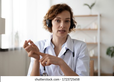 Female Professional Online Doctor Wearing Headset Speaking Looking At Camera Consulting Patient In Virtual Chat. Physician Talking Using Video Call App Consultation. Telemedicine Concept. Webcam View