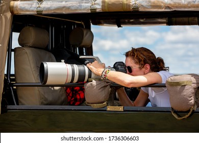 Female Professional Photographer On Safari. Woman Rests Camera On A Bean Bag And Shoots Wildlife From A Safari Vehicle.  In The Masai Mara, Kenya.