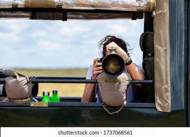 Female Professional Photographer On Safari. Woman Rests Camera On A Bean Bag And Shoots Wildlife From A Safari Vehicle.  In The Masai Mara, Kenya.