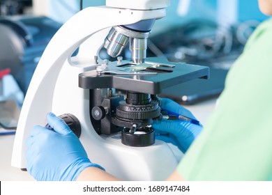 Female professional in uniform. Work with a light microscope in a research laboratory, testing laboratory. Histology, histopathology, microscopic analysis of patients, biopsy with cancer, Covid-19.
