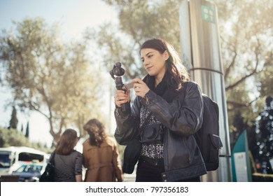 Female professional videographer travel photographer making video in 4K resolution trough of the streets holding 3 axis gimbal stabilizer.Filming with stabilized camera.Travel light equipment