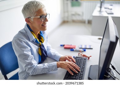 A female professor in front of a computer desk at the informatics lecture in the university computer classroom. Professor working at the college. Education, college, university, learning concept