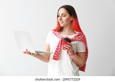 Female programmer with cup of coffee using laptop on light background