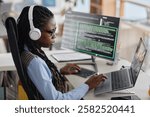 Female programmer deeply engaged in coding while wearing headphones and working with multiple screens in modern office environment