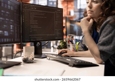 Female programmer seen typing code for a user interface design on dual monitors, working in a digital workspace. Woman IT specialist working on software engineering and front end development.