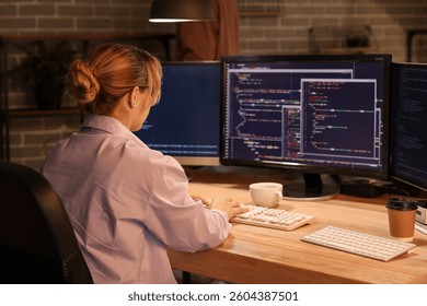 Female programmer working with computer in office at night, back view