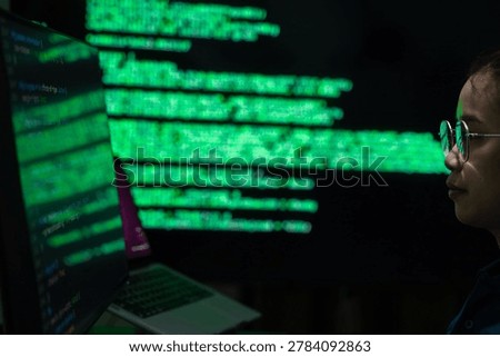 A female programmer working in a dark office environment while monitoring cybersecurity data and digital code on a computer screen. The scene represents software development, cyber technology, data analysis, and information security in a modern technology workspace.