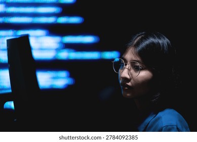 A female programmer working on a computer with illuminated digital information screens in a dark technology office. The image represents software engineering, cybersecurity monitoring, and modern digital workspace environments.