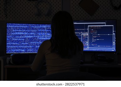 Female programmer working on computer code at night, cybersecurity and software development concept, dark room environment
