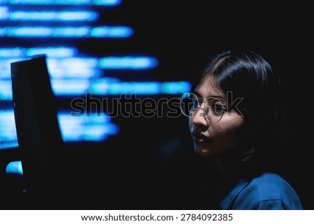 A female programmer working on a computer with illuminated digital information screens in a dark technology office. The image represents software engineering, cybersecurity monitoring, and modern digital workspace environments.