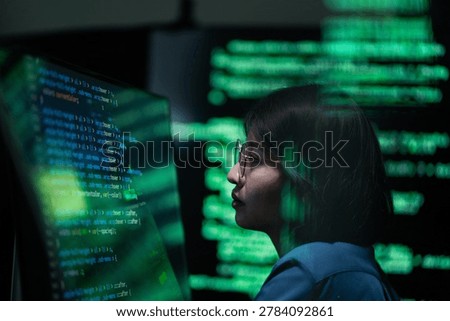 A female programmer working on a computer with illuminated digital information screens in a dark technology office. The image represents software engineering, cybersecurity monitoring, and modern digital workspace environments.