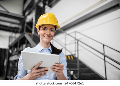 Female project manager standing in modern industrial factory, holding tablet. Manufacturing facility with robotics, robotic arms and automation. Storing products and materials in warehouse. - Powered by Shutterstock