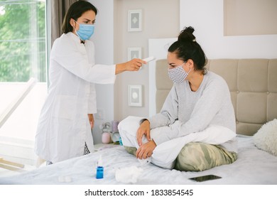 Female with protection mask getting her fever checked by a nurse with with mask and a digital thermometer at home. - Shutterstock ID 1833854545