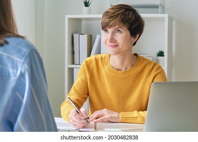 Female Psychologist Coach Talking To Patient And Taking Notes. Professional Session Of Rehab Therapy. Conversation Of Two Ladies About Mental Health Issues. Face-to-face Appointment. Empathetic Doctor