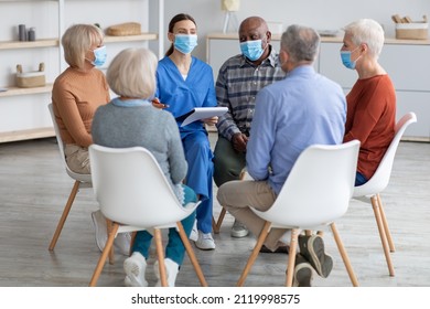 Female Psychologist Having Group Therapy With Senior People Different Nationalities, Elderly Men, Women Sitting On Chairs In Circle, Wearing Protective Face Masks. Nursing Home And COVID-19 Pandemic