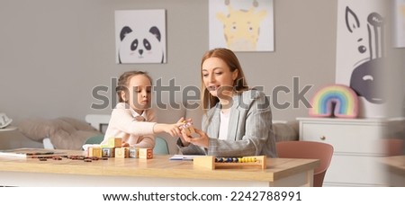 Female psychologist working with little girl suffering from autistic disorder in office