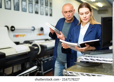 Female publishing facility worker reading operation manual for large printer. Her male co-worker standing beside. - Shutterstock ID 2167178227