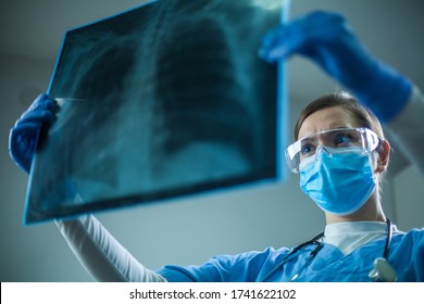 Female pulmonologist or oncologist holding chest X-ray scan,inspecting COVID-19 patient lungs,wearing PPE uniform,Coronavirus acute respiratory new virus disease infection causing breathing problems - Powered by Shutterstock