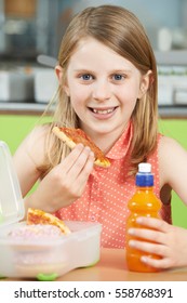 Female Pupil Sitting At Table In School Cafeteria Eating Unhealthy Packed Lunch