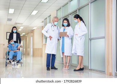 Weibliche, die den Patienten auf den Rollstuhl drängt, wobei drei Ärzte im Krankenhauskorridor sprechen. Konzept der Gesundheitsversorgung, der Reanimation und der Medizin