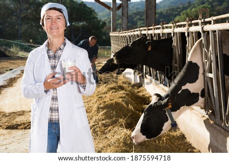Female quality expert is standing in uniform at the cow farm.