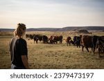Female rancher watches her cattle graze pasture in rural Eastern Washington 