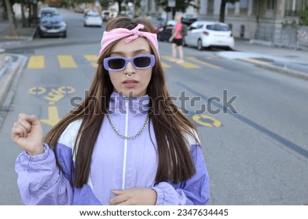 Female rapper wearing purple sunglasses, pink bandana, septum piercing and gold necklace  