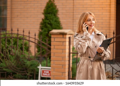 Female Real Estate Agent Talking By Mobile Phone Outdoors