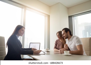 Female Realtor Meeting With Young Couple In Real Estate Agency Office. Discussing First Property Investment With Broker, Construction Company Manager Showing Build Project, Apartment Plan On A Laptop