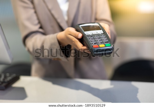 Female receptionist employee holding\
card reader machine on hand at checkout\
counter.