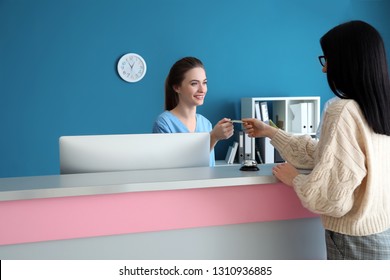 Female Receptionist Receiving Payment For Medical Service From Patient In Clinic