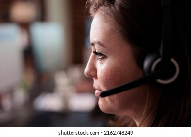 Female Receptionist Wearing Headphones To Work At Call Center Helpdesk, Giving Telemarketing Assistance. Woman Working At Customer Service Support To Help Clients, Telephony Network. Close Up.