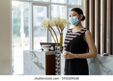 The female receptionist was wearing a surgical mask and holding a tourist thermometer to come to the hotel for service. New normal concept. - Powered by Shutterstock