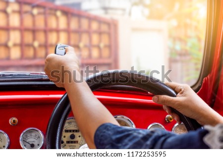 Female in red car, hand holding and using remote control to open the automatic gate while leaving home. Security and save time concept.