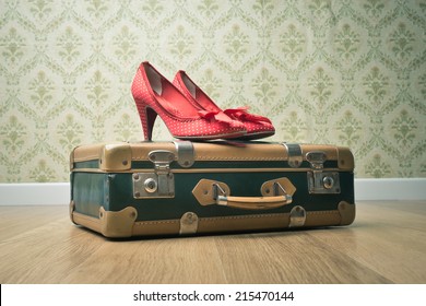 Female red dotted shoes with vintage suitcase on floor and retro wallpaper.