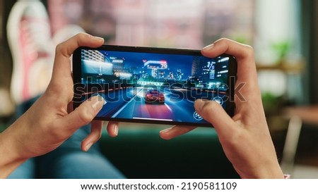 Female is Relaxing on a Couch at Home, Playing an Interactive Racing Drift Video Game on Her Smartphone. Gamer Lies on a Sofa in Living Room. Close Up POV Photo of Mobile Device Screen.