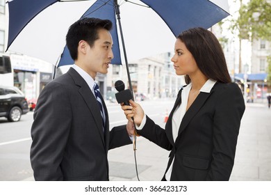 A female reporter interviews a well dressed man holding an umbrella. Could be a politician, businessman etc.