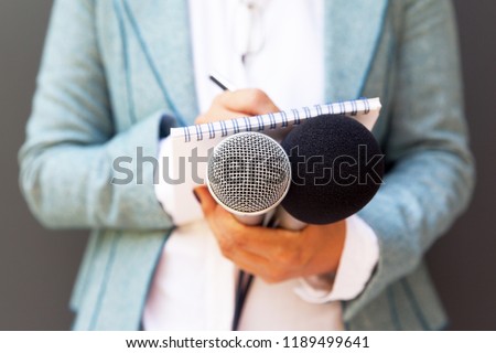 Female reporter at press conference, writing notes, holding microphone