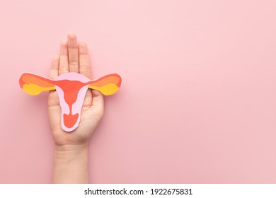 Female reproductive health concept. Woman hand holding uterus shape made frome paper on pink background. Awareness of uterus illness such as endometriosis, PCOS, STDs or gynecologic cancer. 
