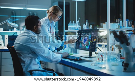 Female Research Scientist with Bioengineer Working on a Personal Computer with Screen Showing Virus Analysis Software User Interface. Scientists Developing Vaccine, Drugs and Antibiotics in Laboratory