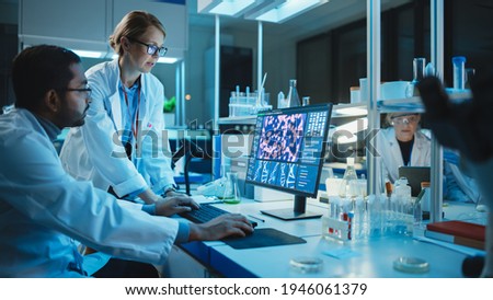 Female Research Scientist with Bioengineer Working on a Personal Computer with Screen Showing DNA Analysis Software User Interface. Scientists Developing Vaccine, Drugs and Antibiotics in Laboratory