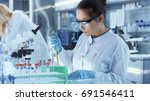 Female Research Scientist Uses Micropipette Filling Test Tubes in a Big Modern Laboratory. In the Background Scientists are Working.