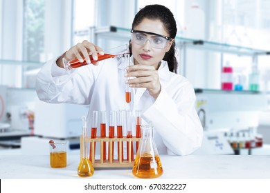 Female researcher doing research in the lab with red and orange chemical liquid on test tube