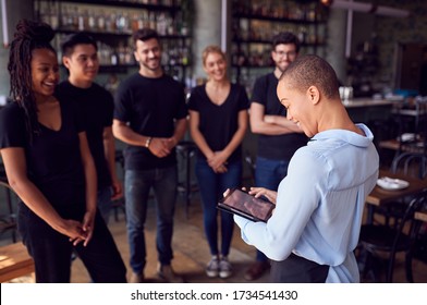 Female Restaurant Manager With Digital Tablet Giving Team Talk To Waiting Staff