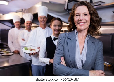 Female restaurant manager standing in front of team of staff smiling at camera - Powered by Shutterstock