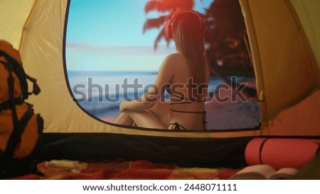 Female resting on campsite relaxing near ocean. Young woman sitting outside the tent at sunset on the beach looking at sea, vacation outdoors.